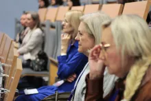 Zbliżenie z profilu na grupę osób, głównie kobiet, siedzących w auli i uważnie słuchających wykładu.