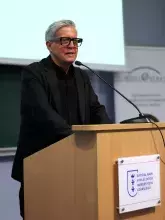 Prof. Treppa w okularach i czarnym stroju stoi za drewnianą mównicą z logo Wydziału Nauk Społecznych Uniwersytetu Gdańskiego i przemawia do mikrofonu.