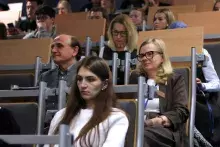 Ujęcie publiczności siedzącej w rzędach auli wykładowej. Uczestnicy konferencji, w różnym wieku, patrzą przed siebie, słuchając prelegenta.