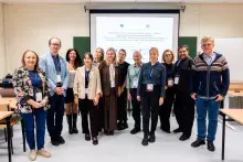 Zdjęcie grupowe jedenastu osób stojących rzędem przed ekranem projekcyjnym w sali konferencyjnej. Wszyscy uśmiechają się do aparatu.