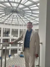 Zdjęcie prof. Rewizorskiego stojącego w kremowym garniturze i niebieskiej koszuli na tle rotundy WNS