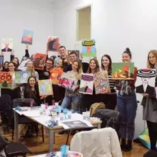 Grupa studentów w sali warsztatowej, prezentująca swoje prace plastyczne