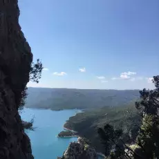 Krajobraz ze stromą skalną ściana na I planie, w tle zatoka w otoczeniu zielonej roślinności